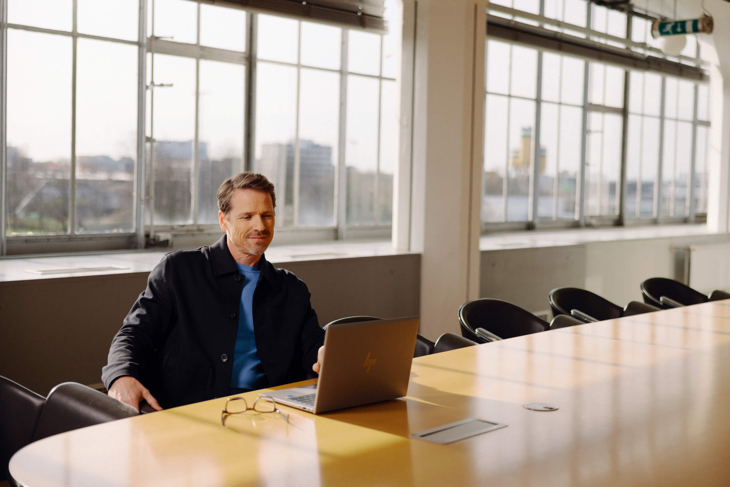 Person Working On Laptop In Bright Conference Room With Large Windows