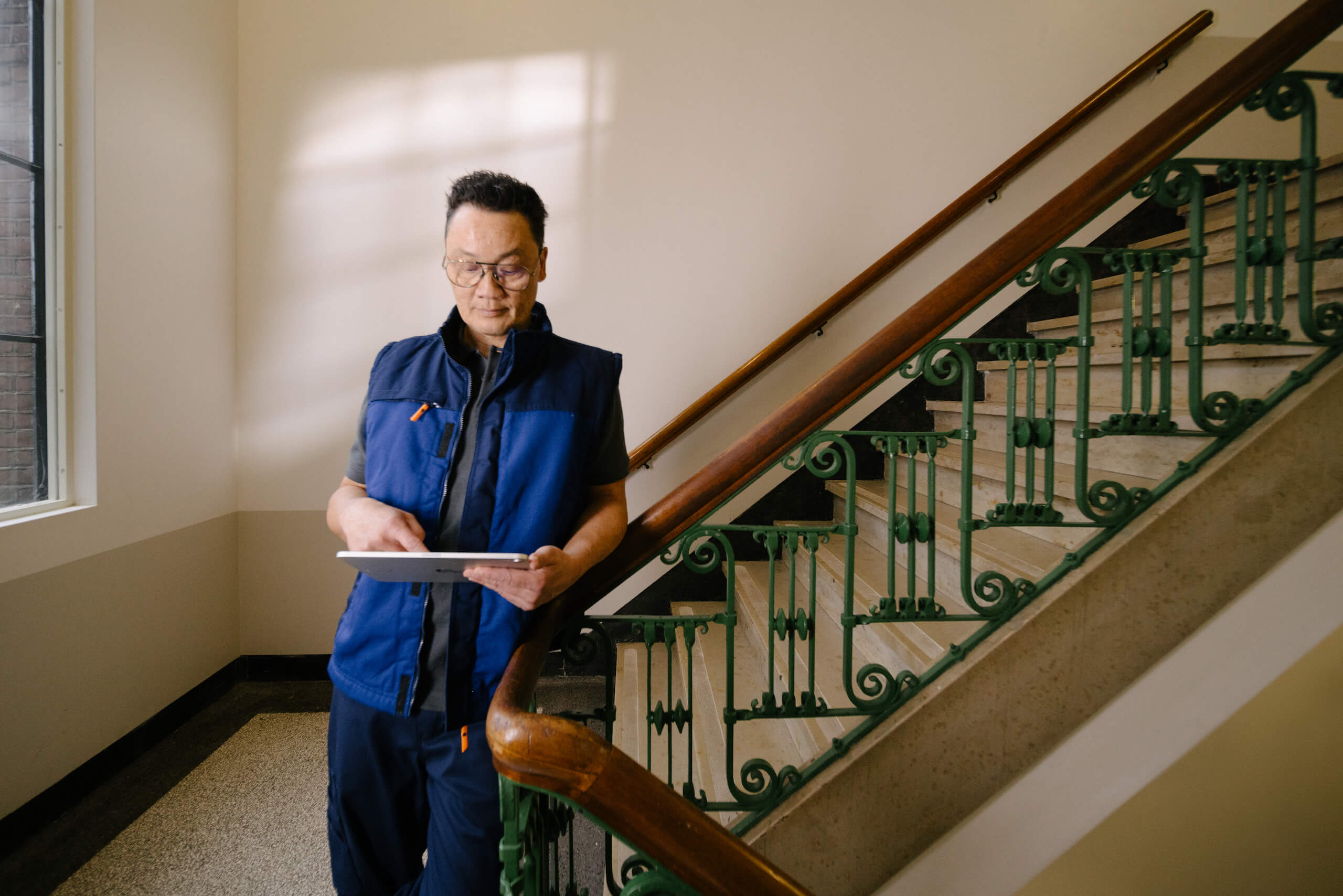 Person Holding A Tablet While Standing Near Ornate Staircase In Bright Interior